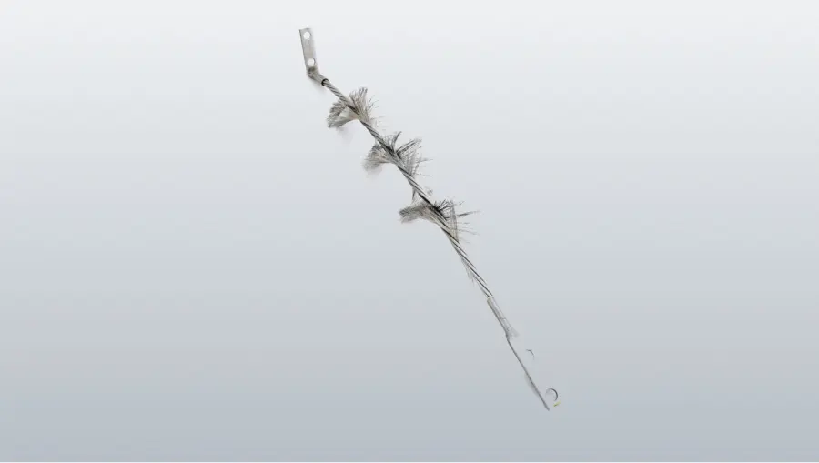 Une brosse métallique torsadée, avec plusieurs touffes de poils gris et des languettes de fixation plates aux deux extrémités, sur fond blanc.