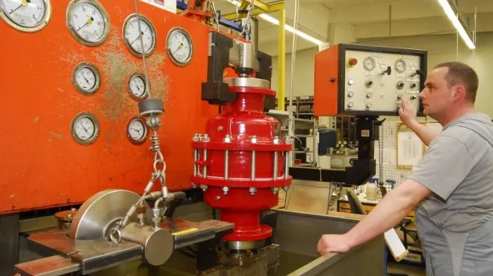 A technician operates a test rig with multiple pressure gauges while a large red industrial valve is mounted on the bench.World’s first in-line detonation arrester type