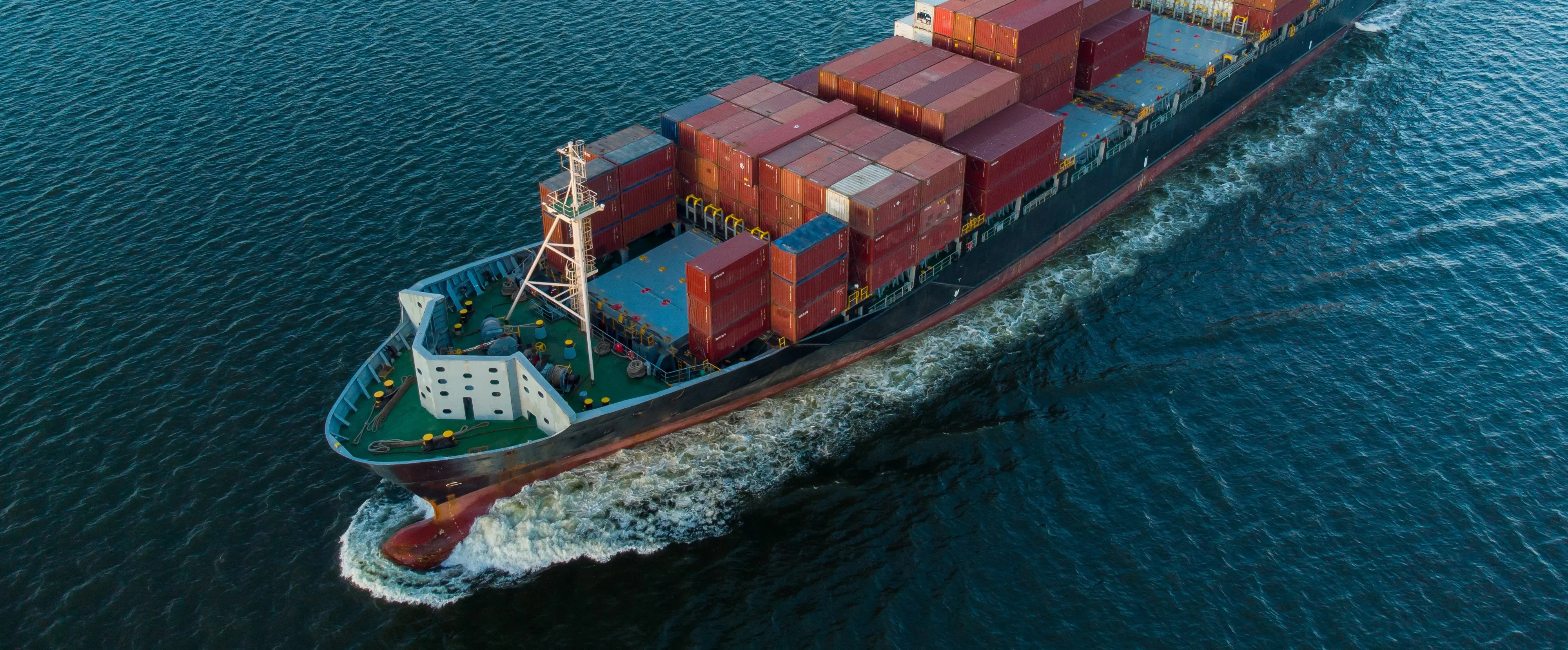 Um navio de carga carregado de contêineres navegando pelo oceano, representando os setores marítimo e offshore