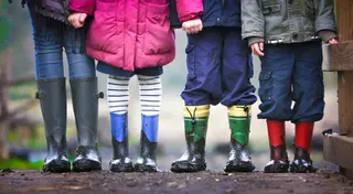 Close-up of an adult and three children standing in muddy wellington boots, showing only their legs and coats.