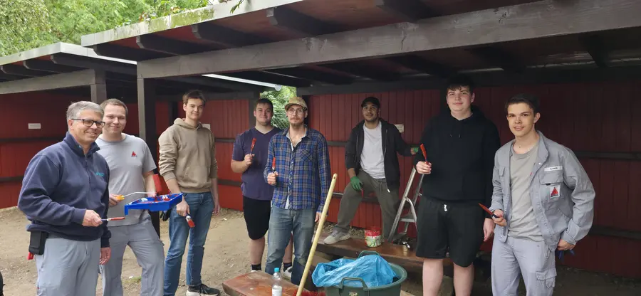 A poster-style collage titled “Brücken bauen” and “PROTEGO Project 2022” shows volunteers holding a long board and planting flowers to create a new outdoor area for a day care centre.