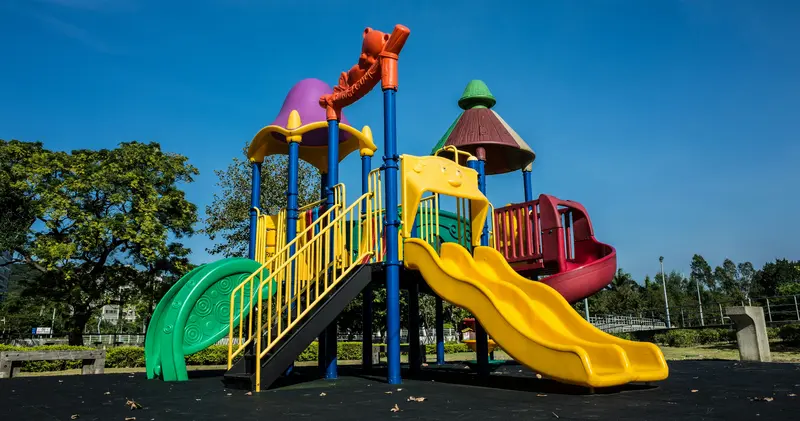 A colorful playground structure with slides and climbing platforms stands under a clear blue sky.