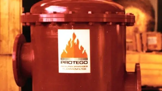 A red industrial cylindrical unit with a “PROTEGO” flame logo label is shown in a workshop setting.