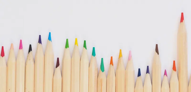 A row of sharpened colored pencils lines the bottom edge of a white background, leaving blank space above.