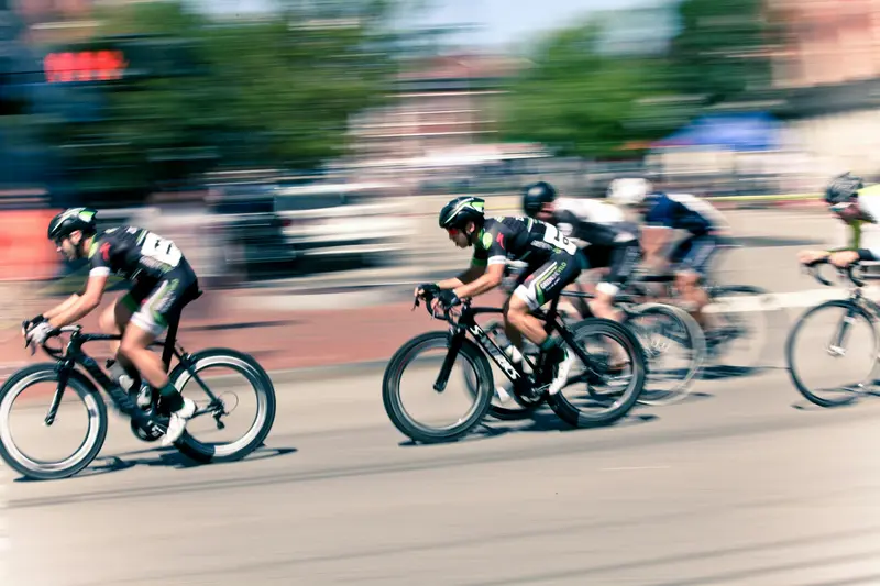 A pack of road cyclists races past with strong motion blur, emphasizing speed on a city street.