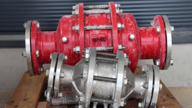 Two industrial inline safety devices or flame arresters, one red and one silver, resting on a wooden pallet with visible frost residue in an outdoor setting.