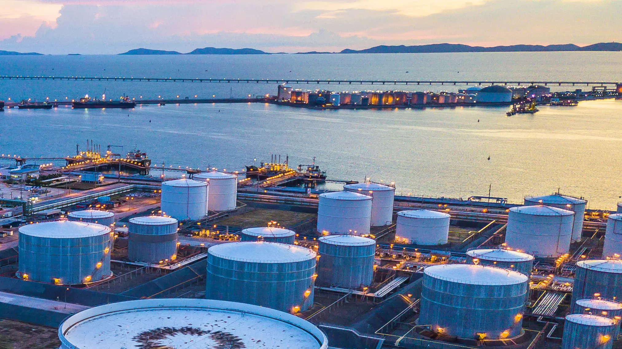 Um complexo da indústria de petróleo e gás com grandes tanques de armazenamento próximo a um porto ao entardecer