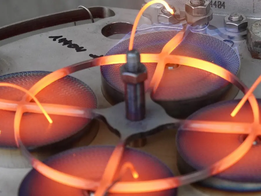 Close-up of a laboratory test device with glowing heated wires and circular metal elements, showing an active high-temperature experimental setup.
