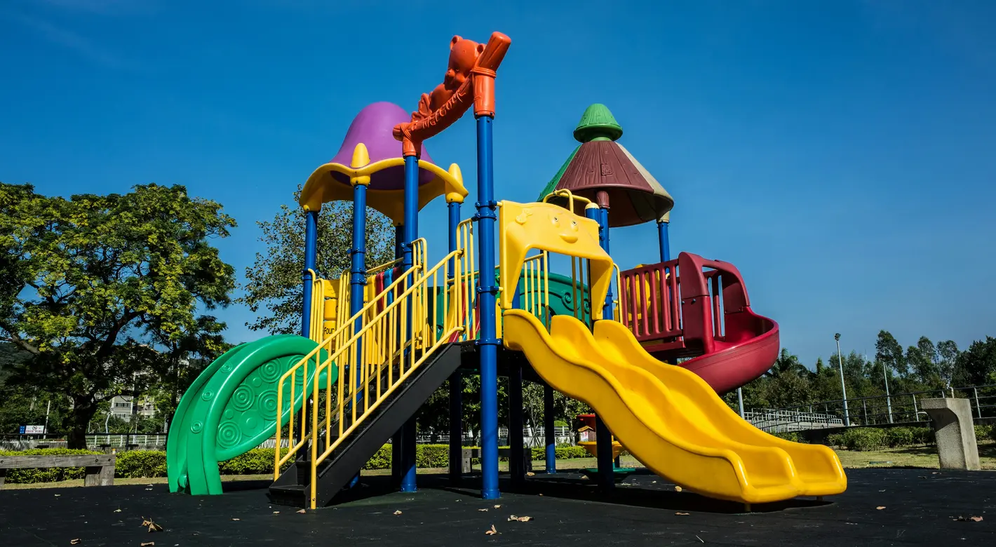 A colorful playground structure with slides and climbing platforms stands under a clear blue sky.